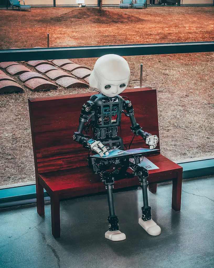 A robot hand and a human hand reaching for the letters AI